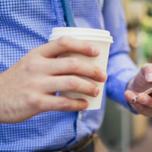 man holding cell phone and coffee